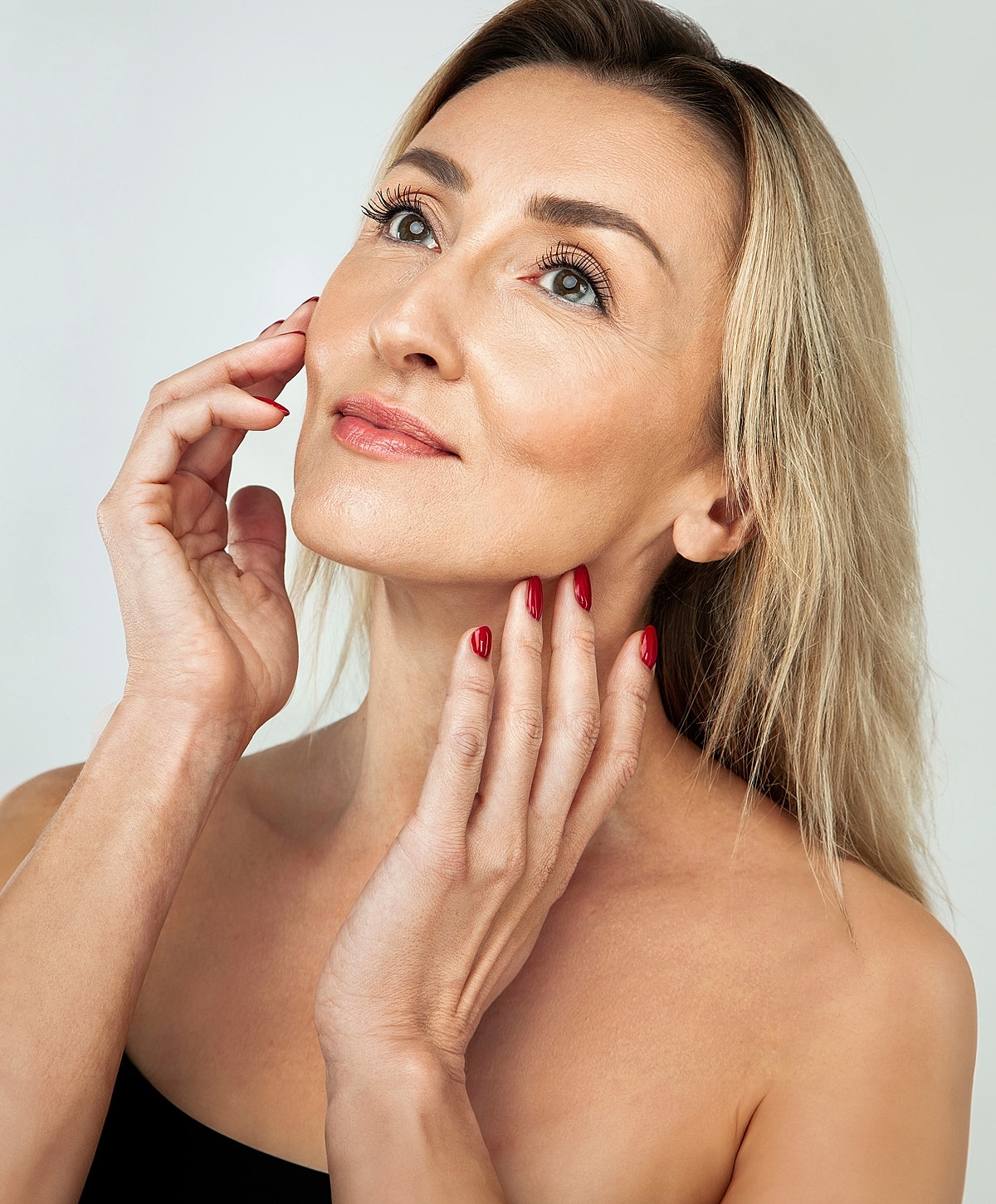 Woman with blonde hair and red nails looking up.
