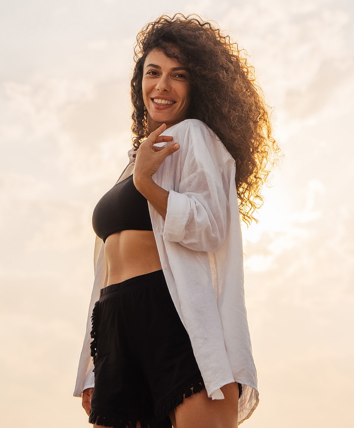 Smiling woman in casual beach attire at sunset.