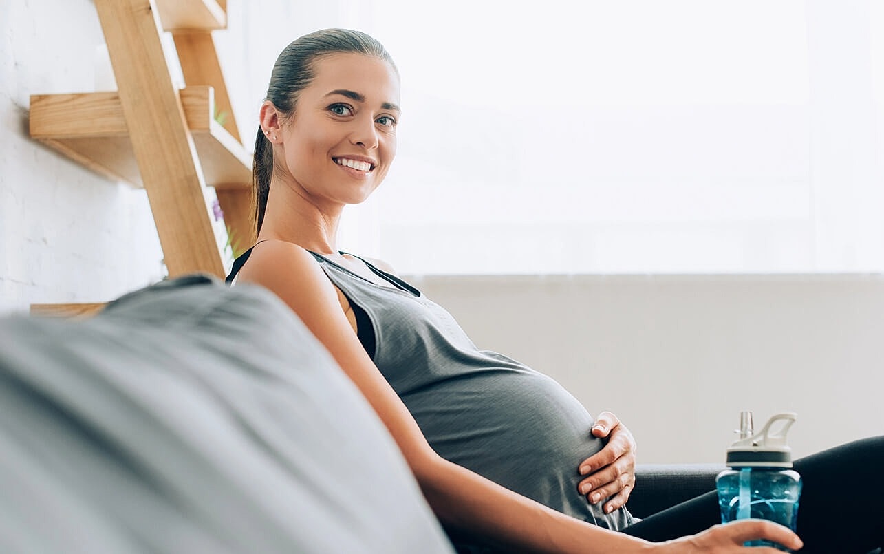 Pregnant woman relaxing on couch with water bottle.