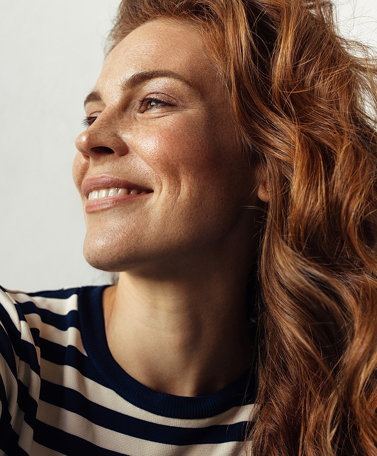 Woman with wavy red hair smiling softly.