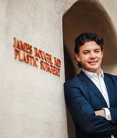 Plastic surgeon by entrance sign, smiling confidently.