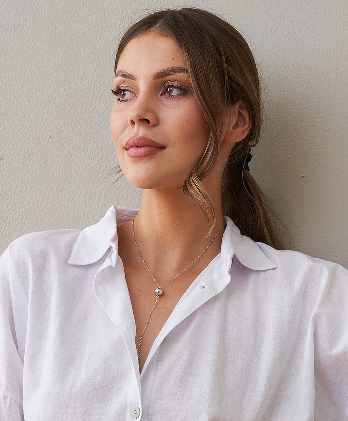 Woman in a white shirt, wearing a necklace.